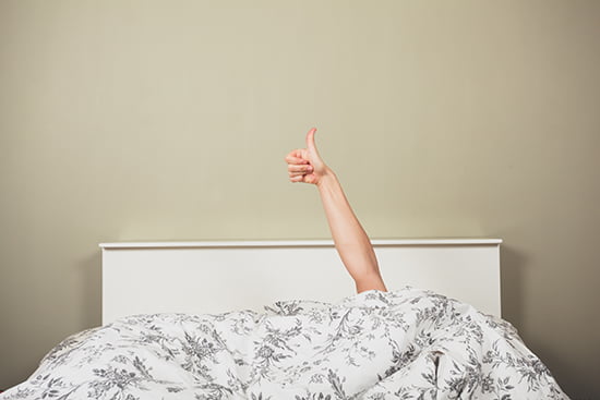 A young woman in a bed is giving thumbs up